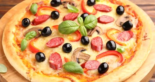 Tasty pizza with smoked sausages, mushrooms and black olives on table, rotating