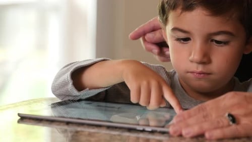 Child using tablet device with guiding hand indoors