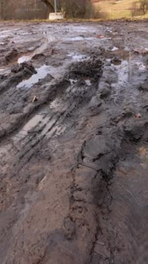 Vertical close-up of deep muddy vehicle ruts with standing water on a damaged countryside path,