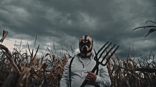 Scary Figure in Mask with Pitchfork in Cornfield