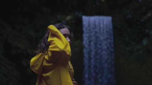 Woman Unzipping Rain Jacket by Waterfall