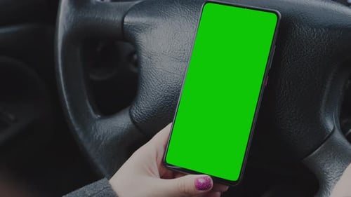 Wman's Hand Holds Phone Against Background Steering Wheel In Car