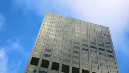 Wolken und blauer Himmel spiegeln sich an den Fenstern eines Gebäudes, wenn sie vorbeiziehen