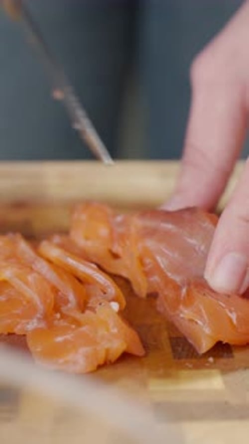 Slicing raw salmon fillet with knife on wooden cutting board
