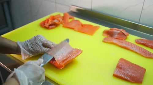 Cutting red salmon into pieces during cooking with hands in white gloves, close up. Slow motion.