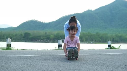 Mother teaching her daughter how to skateboard in the park. Child riding skate board.