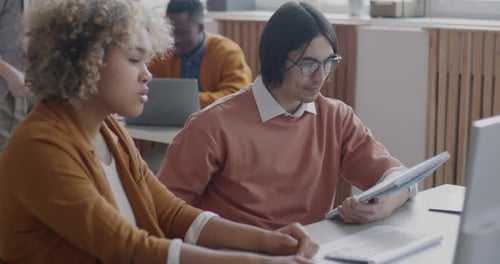 Man and Woman Colleagues Talking Looking at Computer Working Together in Shared Office