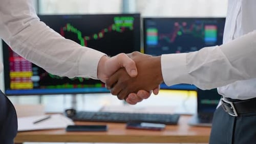 Close Up of Two Diverse Traders Handshake with Candlestick Forex or Cryptocurrency Chart on Blurry
