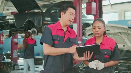 A male automotive supervisor and a Black female mechanic work in a car garage.