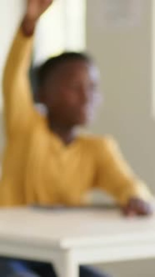 Vertical video: Camera focusing pupil in yellow top raising hand answering in class at desk tablet