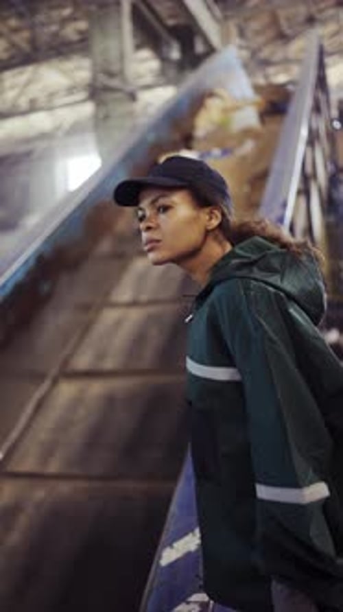 A Young AfricanAmerican Woman Checks a Conveyor Belt at a Recycling Plant Pollution Control