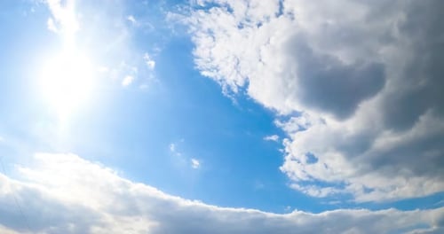 Strahlende Sonne am blauen Sommerhimmel. Eine große graue Wolke nähert sich, um die Sonne zu verbergen. Ansicht von unten.