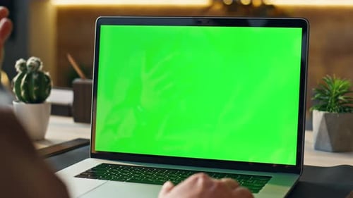Person typing on laptop with green screen at desk