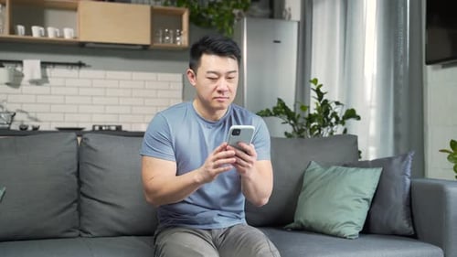 Young Adult Using Cell Phone Indoors on Sofa