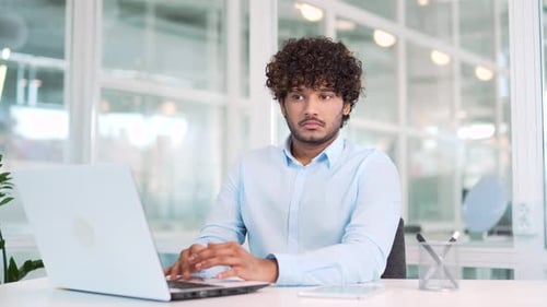 Man Shrugs While Typing at Laptop in Office