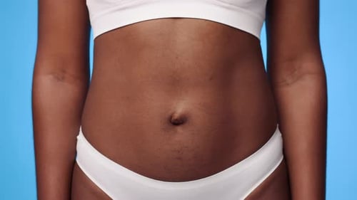Junge Afroamerikanerin zeigt Bauch vor hellblauem Hintergrund
