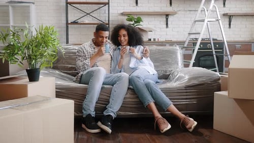 Slow Motion Couple Sitting on Sofa Surrounded By Packed Cardboard Boxes Drinking Coffee or Tea