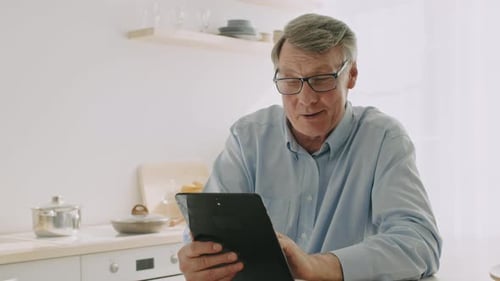 Senior Man Uses Tablet in Bright Kitchen