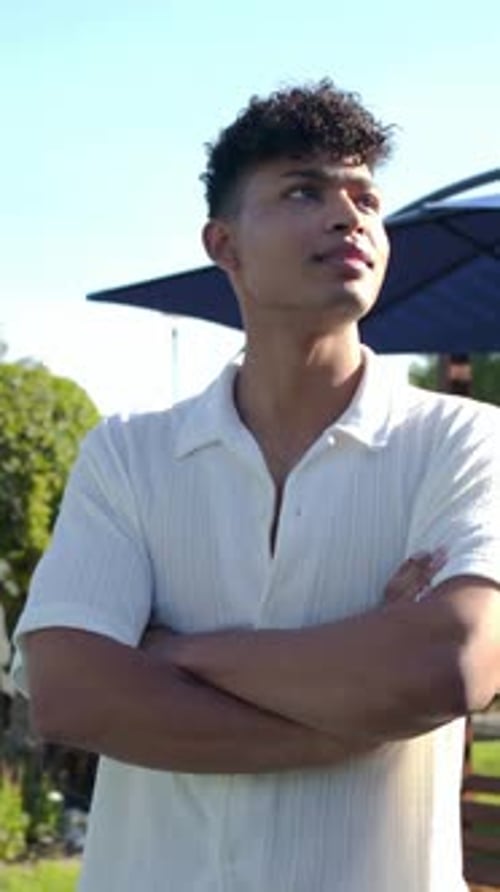 Vidéo verticale : Remarquant le bon mouvement, faisant tourner un homme en chemise légère souriant dans le jardin avec un parasol