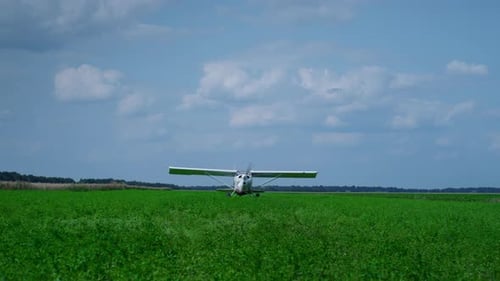 Lightweight Airplane with Spinning Propeller Parking on Green Field Cloudy Day. White