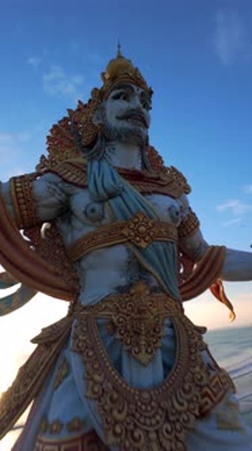 Vol cinématographique en Drone FPV autour d'une statue géante en bord de mer au coucher du soleil à Bali