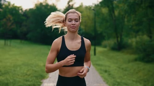 Female Runner is Jogging in the Park Wearing Sport Clothes and Smartwatch