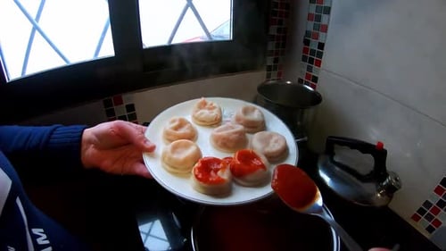Woman putting tomato sauce with a spoon, Italian pasta (Sorrentinos) in the kitchen