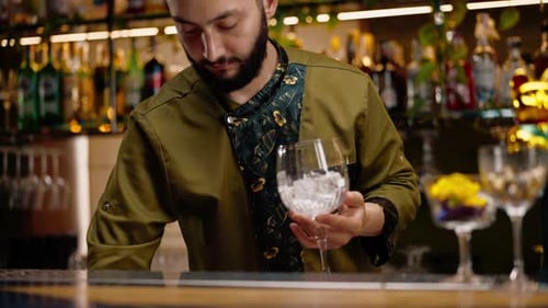 close-up of a bartender pours ice cubes into a cocktail glass in preparation of delicious cocktails