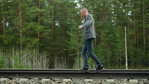Man Balancing on Railway Tracks in Grey Suit and Blue Jeans in a Serene Forest