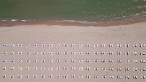 A Sandy Beach Stretches Along the Seaside Adorned with Empty Sun Loungers Aerial View