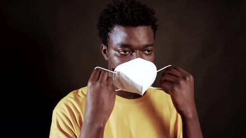 Young Black Man Putting On N95 Face Mask For Coronavirus Protection. medium shot