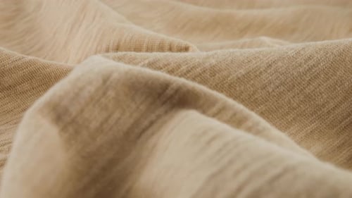 Close-up view of the soft folds of the thin beige cotton jersey. The textile background rotates