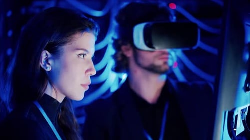 Woman programming in a server room while a man is using a Virtual Reality headset