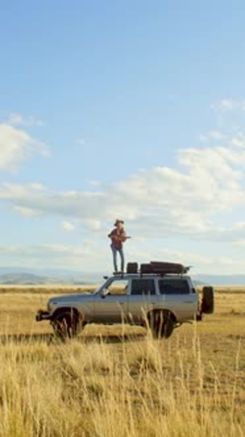 Person Standing on Top of SUV in Rural Field