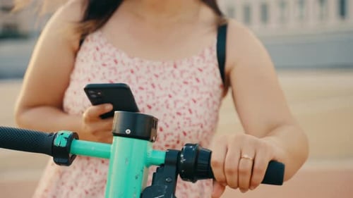 Woman Using Smartphone Next to Scooter Outdoors