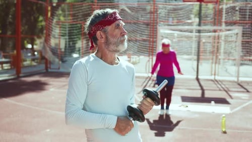 Senior Man Holds Dumbbell at Outdoor Court