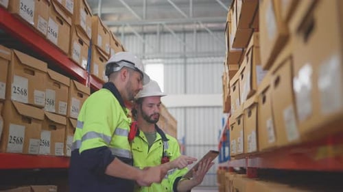 Two professional warehouse worker men hold tablet and discuss about work together