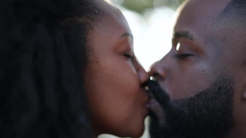 Affectionate African couple kissing outside in slow-motion at park with lens-flare