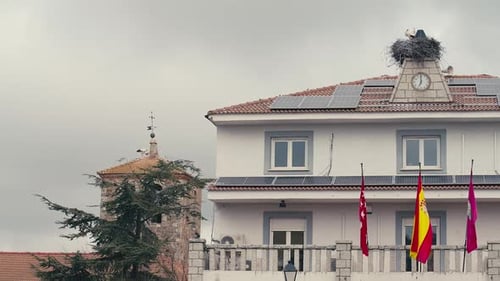 Bâtiment dans une ville espagnole avec des drapeaux et des cigognes sur les toits par un matin nuageux, plan large, calme