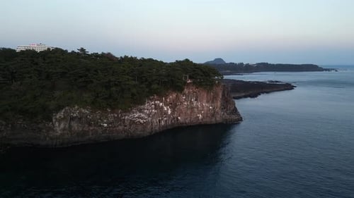 Drone aerial view in South Korea near a cliff over the ocean with green trees over rocky area city b