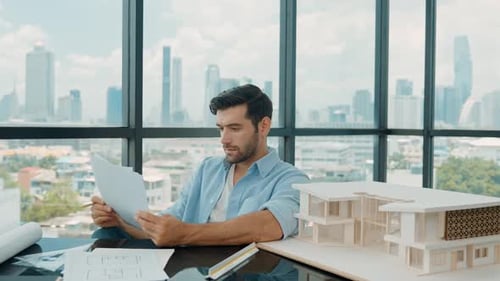 Architect Reviewing Blueprints in Office with City View