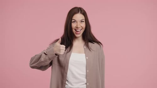 Enthusiastic Woman Gives Two Thumbs Up on Pink Backdrop