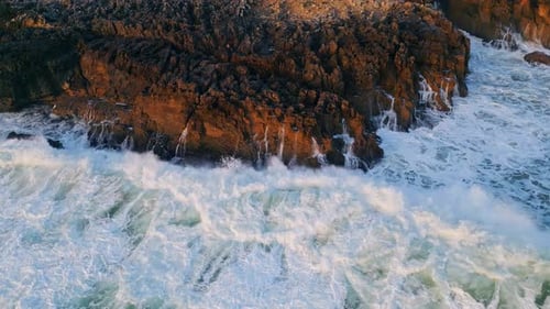 Dramatic aerial view of stormy ocean waves crashing on dark coastal rocks