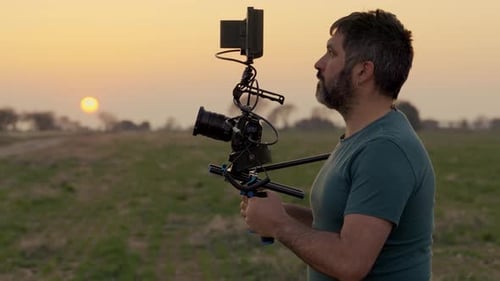 Man Holds Camera in Rural Field at Sunset
