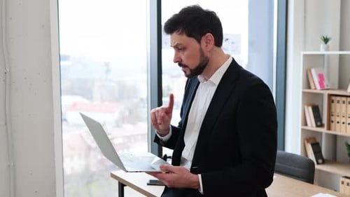 Businessman Smiling During Video Call Holding Laptop in Office Environment