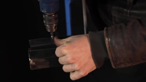 Close up of an electric drill spinning a metal screw into a clamped bar of metal with the person hol