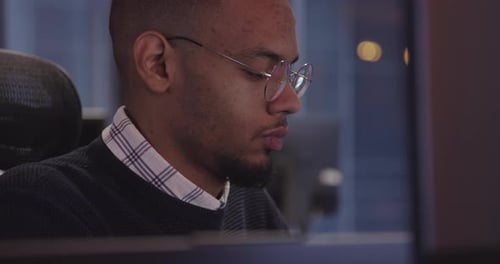 Young African American with Glasses Sitting in a Modern Coworking Office and Working at a Computer