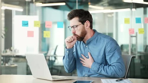 Tired businessman coughing sitting at workplace at desk in business office. Sick with a cold or flu