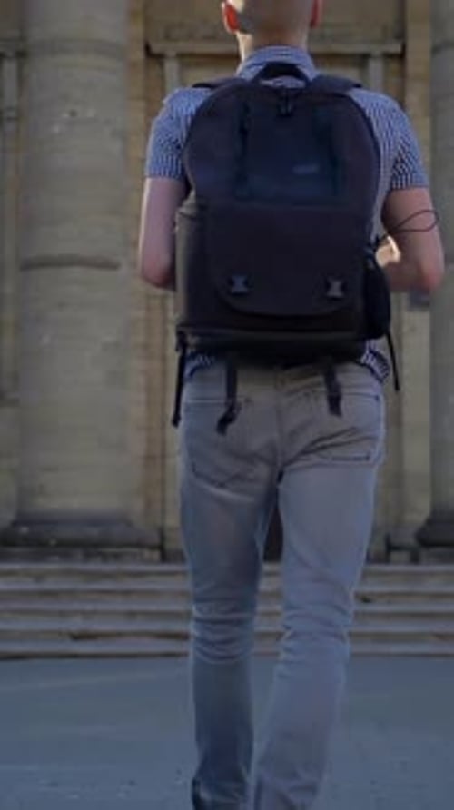 Vertical of A Back Viev of a Young Photographer Who is Approaching an Old Church with an Expensive