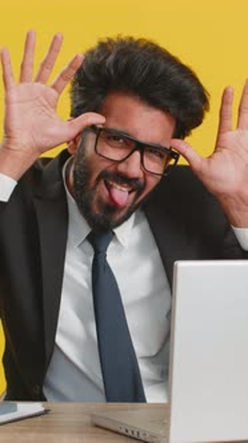 Bürokaufmann versteckt sich hinter einem Laptop und macht ein lustiges dummes Gesicht, das Respektlosigkeit zum Narren hält